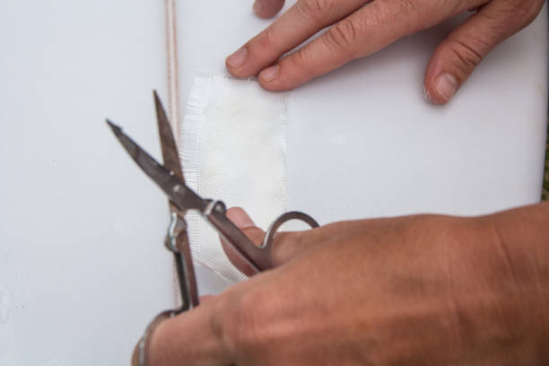 Крупный план рук, разрезающих ткань ножницами рядом с куском ткани, приклеенным к плоской поверхности.